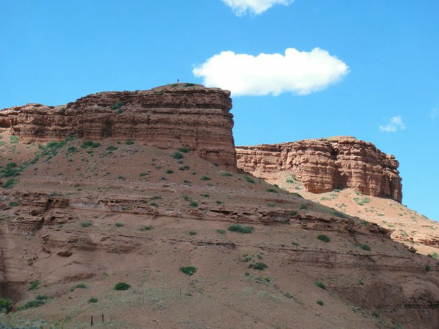 A barely visible man on top of a large red dirt mountain.