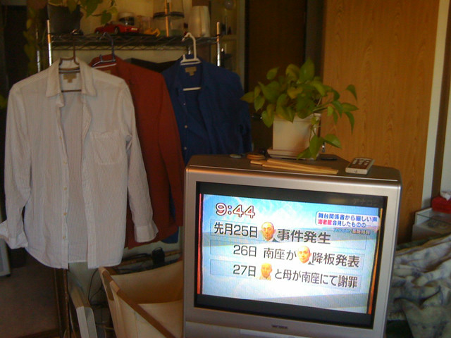 A generic apartment. The TV is on the weather channel, and three striped shirts hang from a hanger.