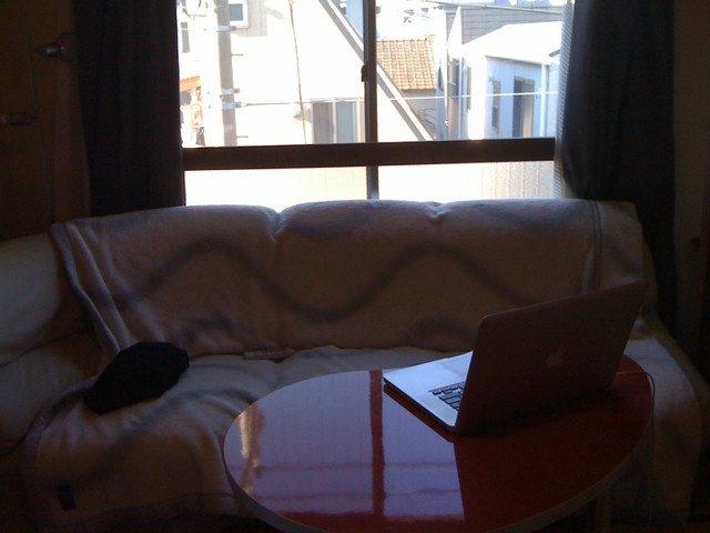 A white couch in a living room. A blanket is strewn over the couch. A Macbook sits on a table in front of the couch.