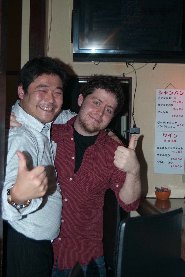 A man in a red striped shirt poses with a salaryman in Japan.