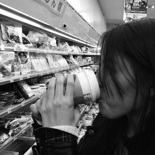 A woman stands in a convenience store, drinking a Starbucks coffee.