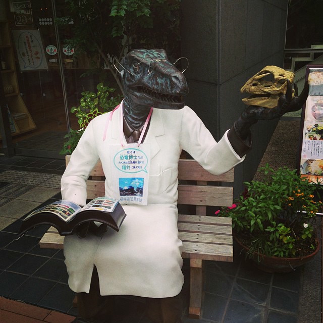 A dinosaur scientist statue, staring at a dinosaur skull. Very meta.