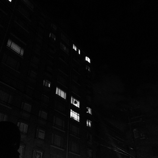 A large building at night, pitch black, with a few select lit up windows.