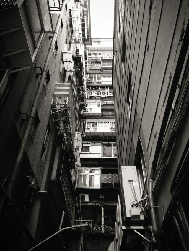 Looking upwards in an alleyway. Various Air Conditioning units and grates block the way.