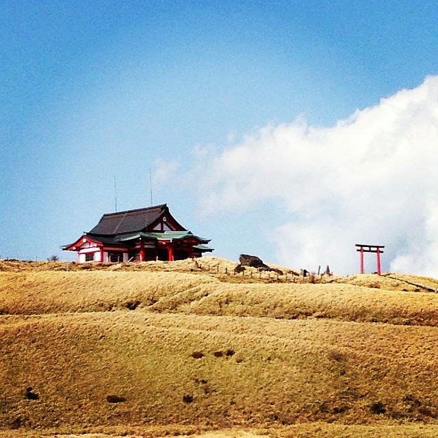 A temple sits atop a mountain in Hakone, Japan. Blue skies and amber hills.