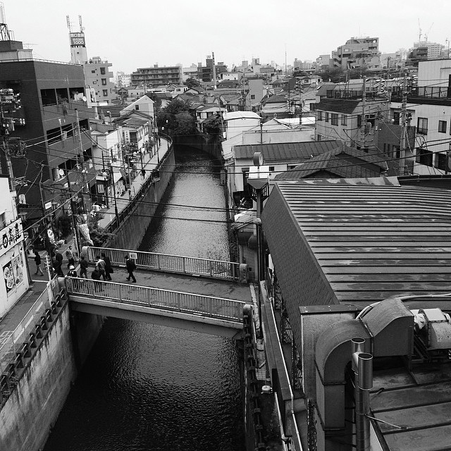     Looking down on a neighborhood cityscape.
    A canal splits the view, with people milling about.
