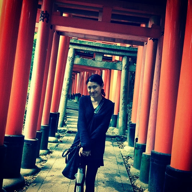 A woman stands in the center of a vortex of Japanese torii gates.