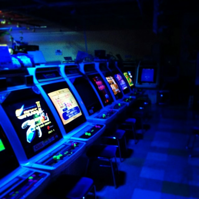 A row of dimly lit arcade machines in a very dark underground arcade.