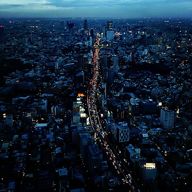 An expansive shot of the Tokyo skyline, with a long line of cars on a freeway cutting the photo in two.