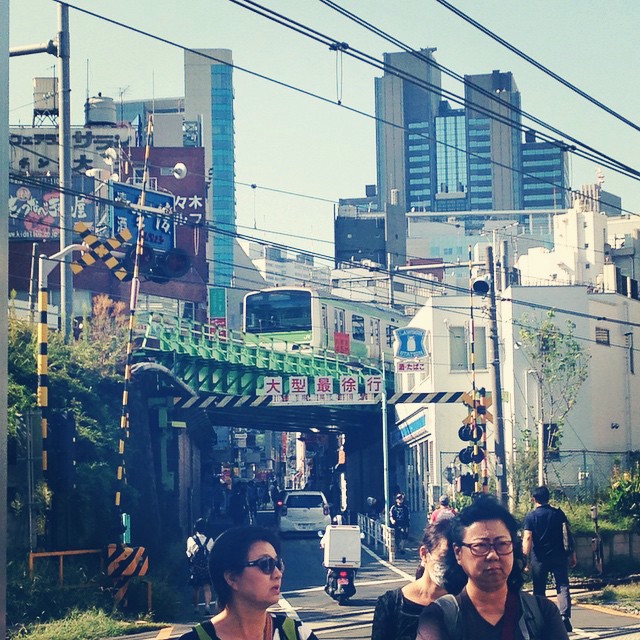 A train moves through a busy Tokyo street as people mill about.