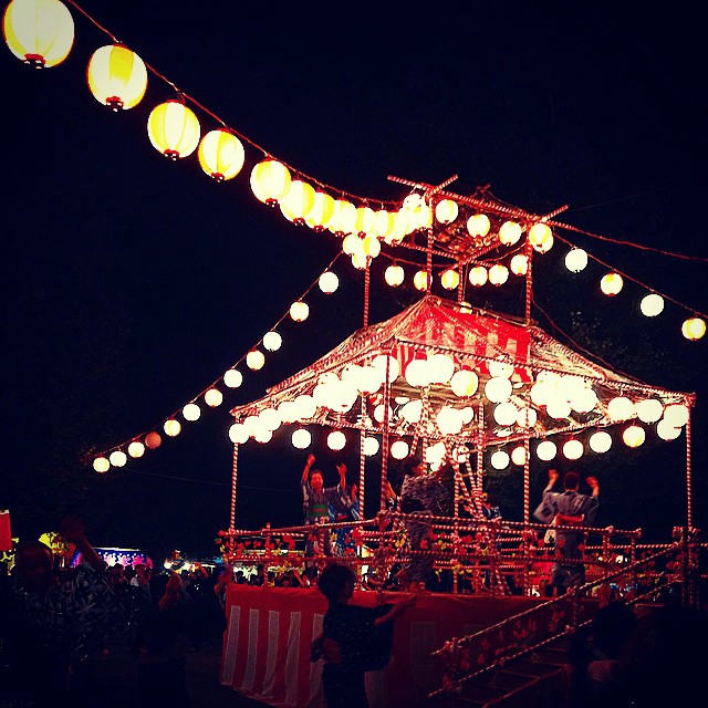 A festival with a red central stage. Food stalls line the area.