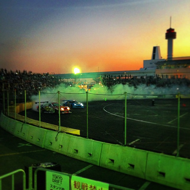 The sun sets as crowds cheer on finalists who tandem drift around a track.