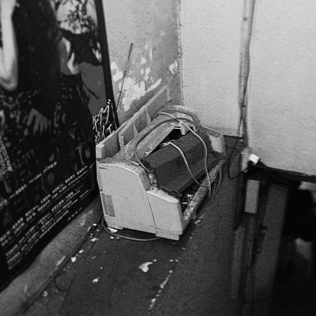 A broken printer sits on a shelf in a derelict building.