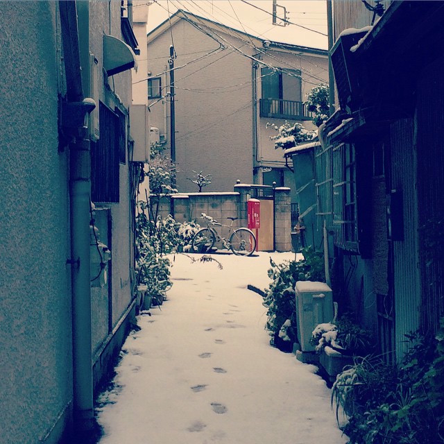 Staring down an alleyway with light snow on the ground. A red postbox is at the end of the alley.