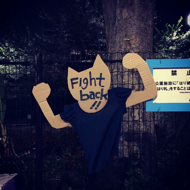 A cardboard cutout art piece. The design is a humanoid cat with a blue shirt, and the words 'fight back' are on the head.