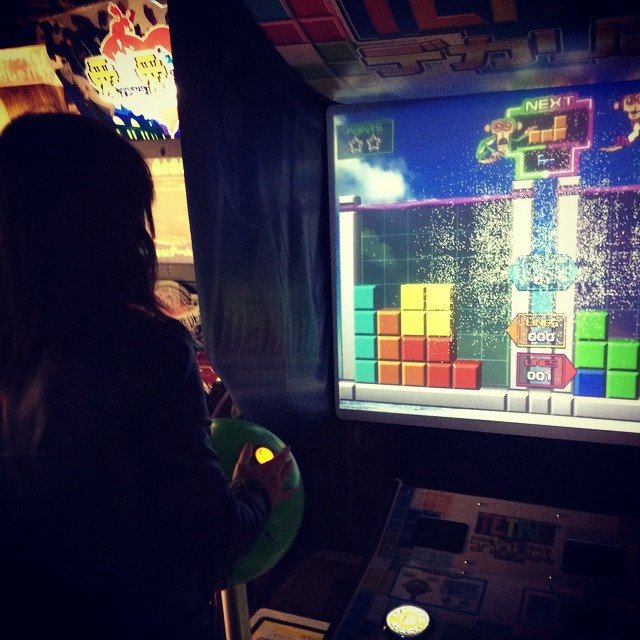 A woman playing a large Tetris game in an arcade, complete with massive joystick.