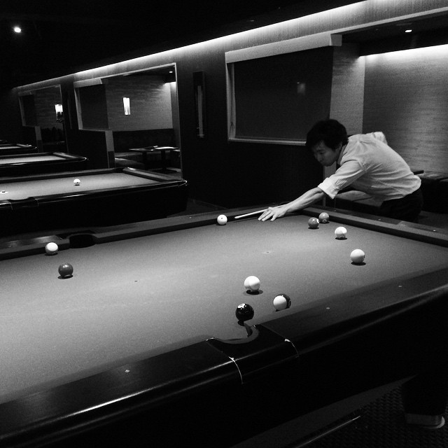 A billiards table in a dimly lit underground pool hall. A man is lining up a shot.