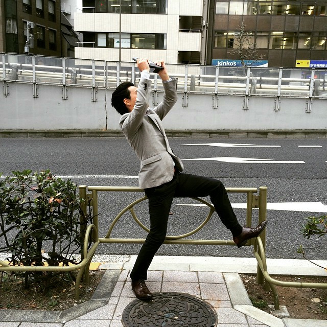 A man leaning on a rail to get a specific camera angle of a building.