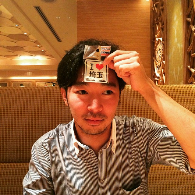 A man holding an i-heart-saitama sticker to his forehead.