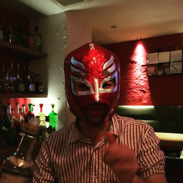 A drunk man in a red luchador mask, holding a bottle of tequila.