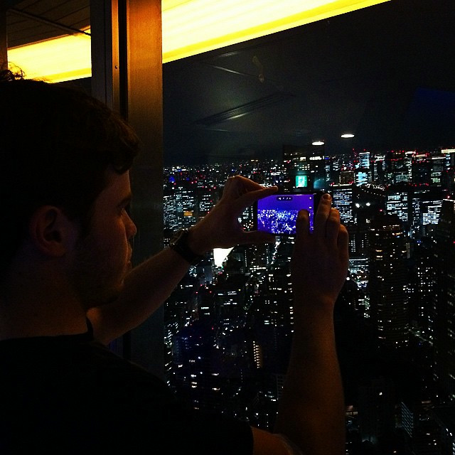 A photo of a man at the top of Tokyo Tower, taking a photo of the Tokyo expanse and skyline at night.