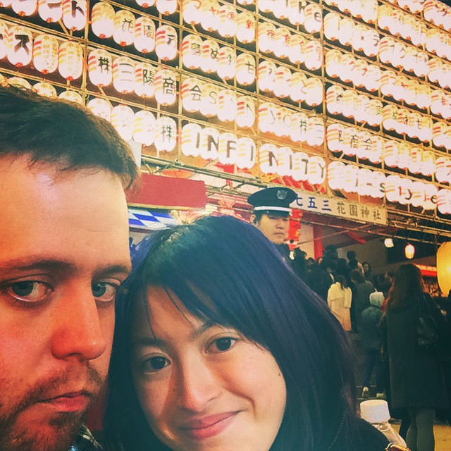 A man and a woman take a selfie in a festival. A cop in the background looks on disapprovingly.