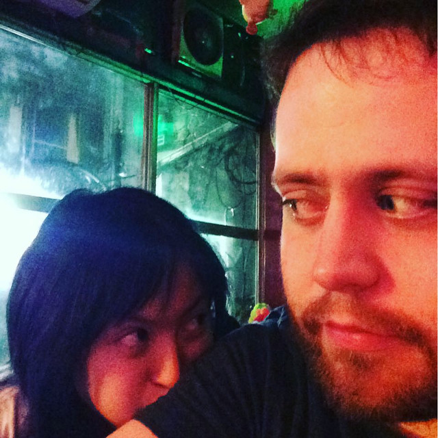 A man and a woman in a bar taking a selfie. The woman has her face buried in the mans shoulder.