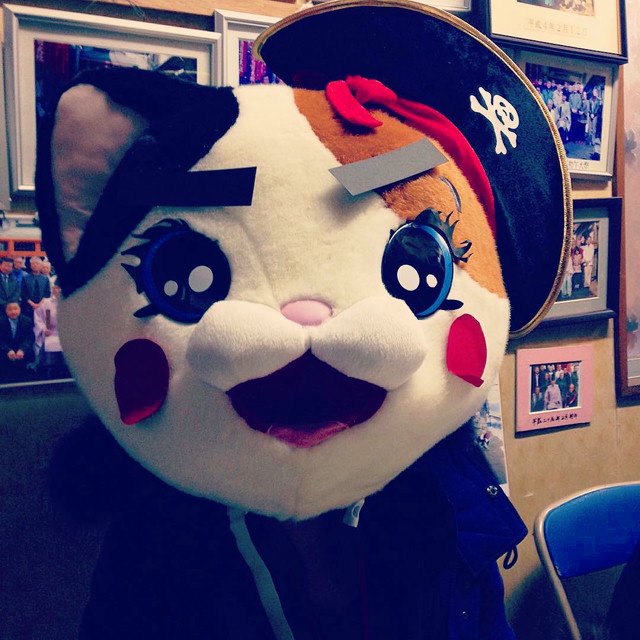 A woman in a blue jacket wearing a cat mascot head mask.