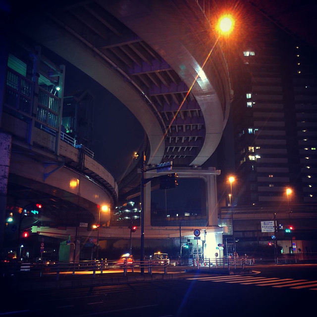 An intersection on a main road in Tokyo. An overhead freeway pass carves to the left.