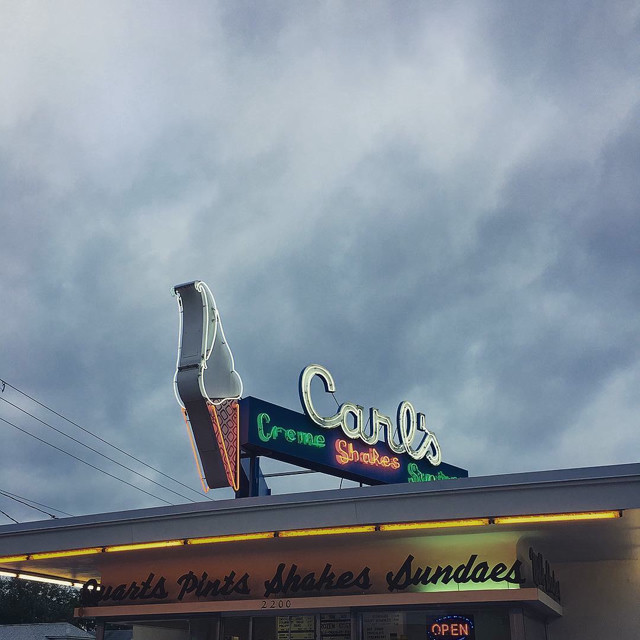 A neon-light ice cream sign that says 'Carls Creme Shakes Sundaes' on top of a building.