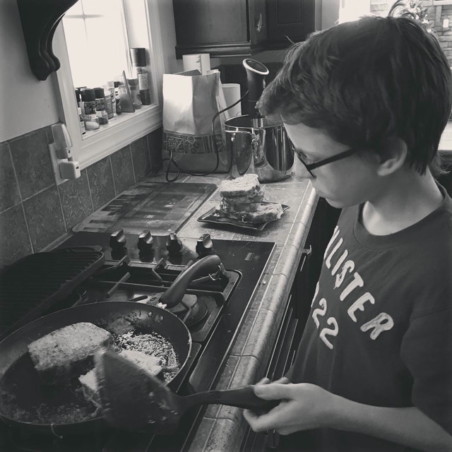 A boy stands over a batch of French Toast he's making.