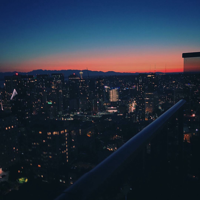 Sun setting over the Seattle skyline. The Space Needle is visible in the distance. The sunset is a blue and orange gradient.