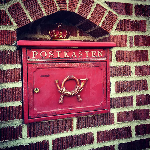 A red postbox embedded into a brick wall. The postbox has the label 'POSTKASTEN'.