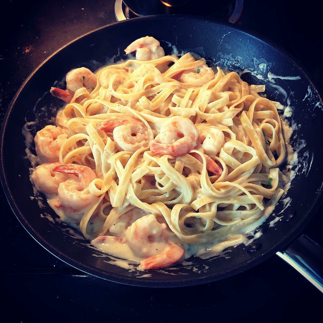 Creamy fettucine alfredo in a pan tossed with shrimp.