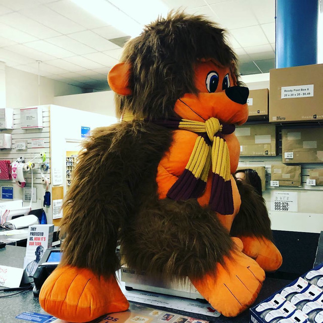 A large stuffed cartoon gorilla sits on a scale in a FedEx office.