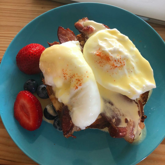 Eggs benedict with fruit on the side. Plated on a blue plate.