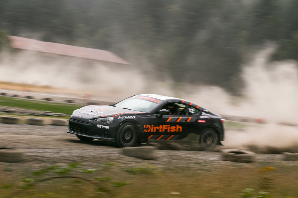 A black car with orange highlights rockets out of a turn. A full dust trail can be seen indicating the path it took before the turn.