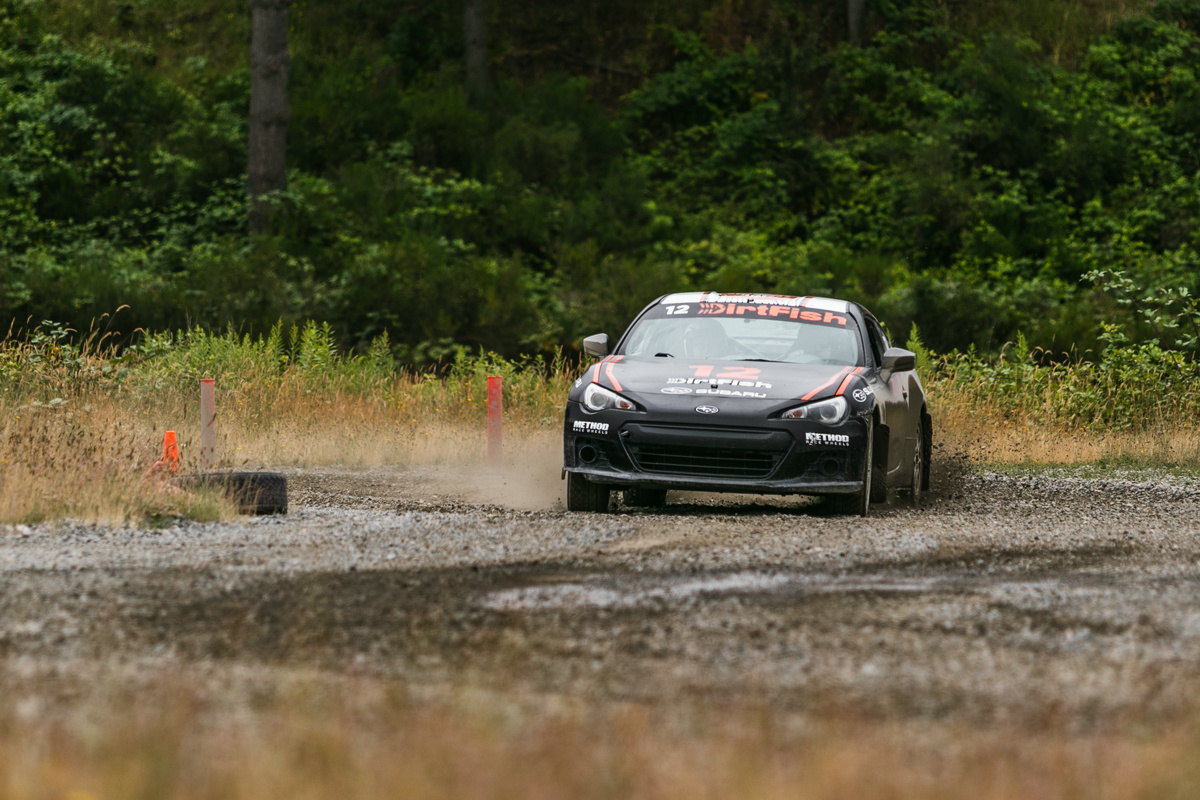 A black coupe with orange highlights finishes a slide out of a wooded area.