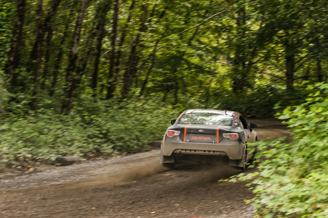 A black car with orange highlights turning on to a wooded path at high speed.