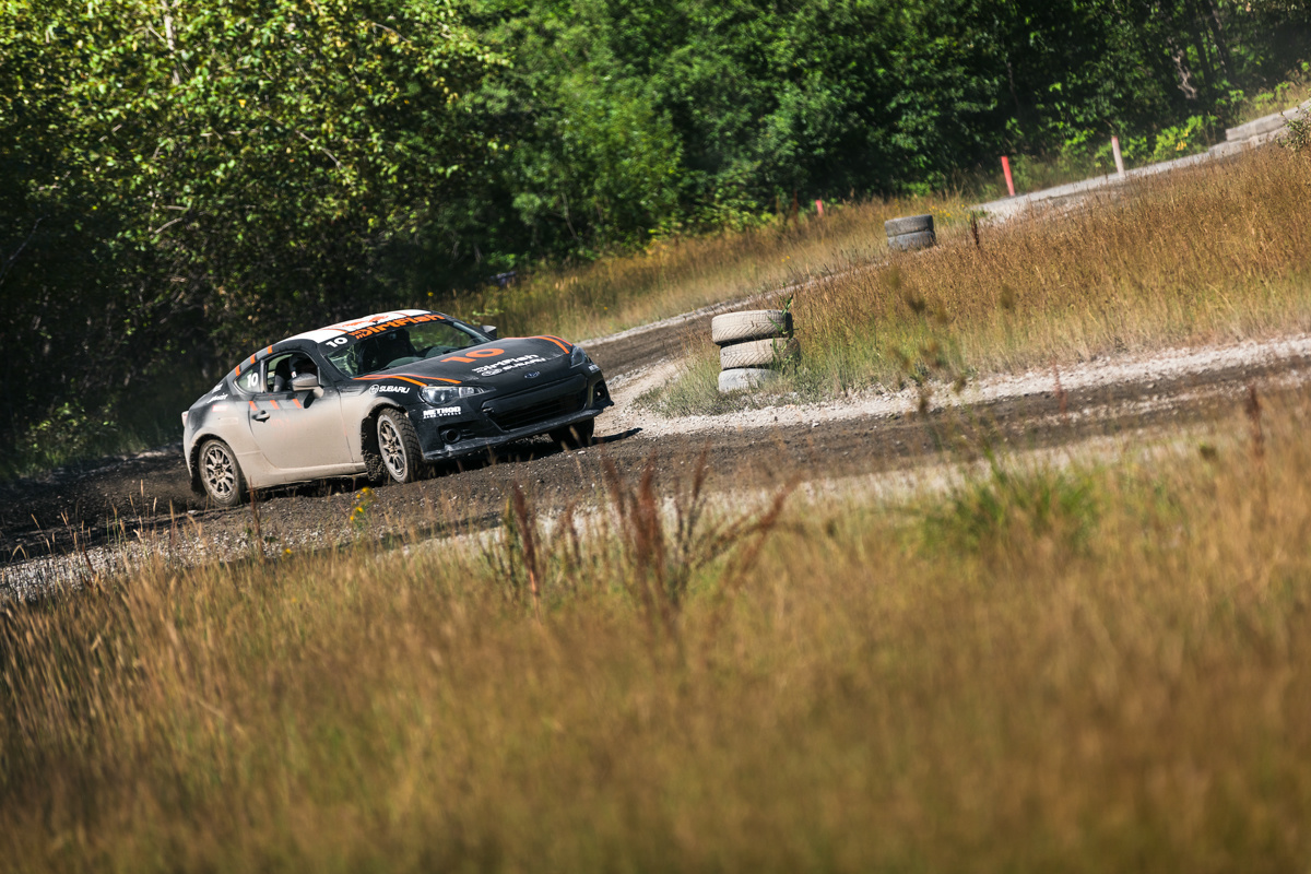 A black car with orange highlights is sideways coming out of a turn. There's a patch of dry gravel on the left side of the car, and the driver is trying to get towards it.