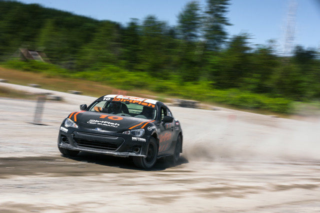 A black car with orange accents slides through the dirt.