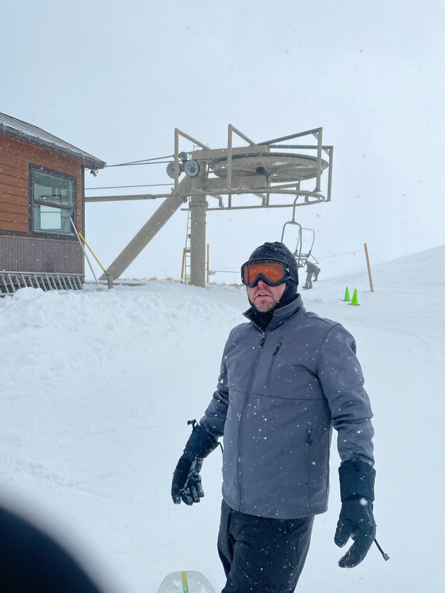 Photo of myself outside of a lift chair on top of a mountain. White-out conditions. I'm wearing a ski goggles (abnormal for me) and light blue/gray snowboarding apparel.