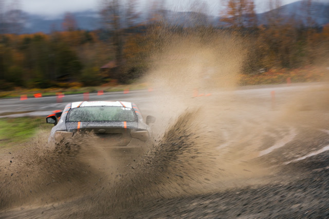 A black car with orange highlights kicks up a wild amount of dirt and muck as it aggressively throttles through a turn.