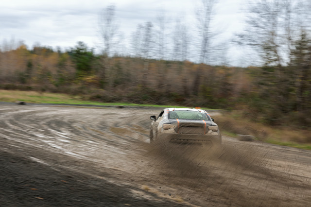 A black car with orange highlights sliding through a right hand sweeping turn.