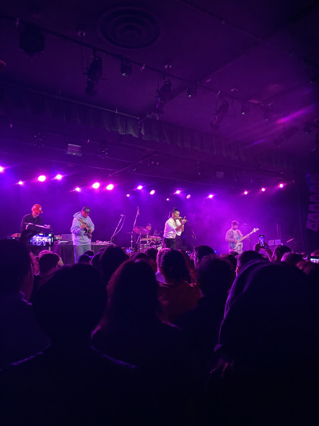 Shing02 and a backing crew performing for an audience. The lights are purple.