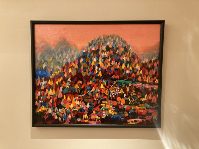 A colorful painting hanging on a wall. The painting is a veritable assortment of colors depicting a field and a mountain.