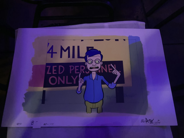 Animation cel from the cartoon named Mission Hill. The scene on the cel is a character standing in front of a sign and pointing upwards. The character has blue hair, glasses, a blue shirt and green pants.