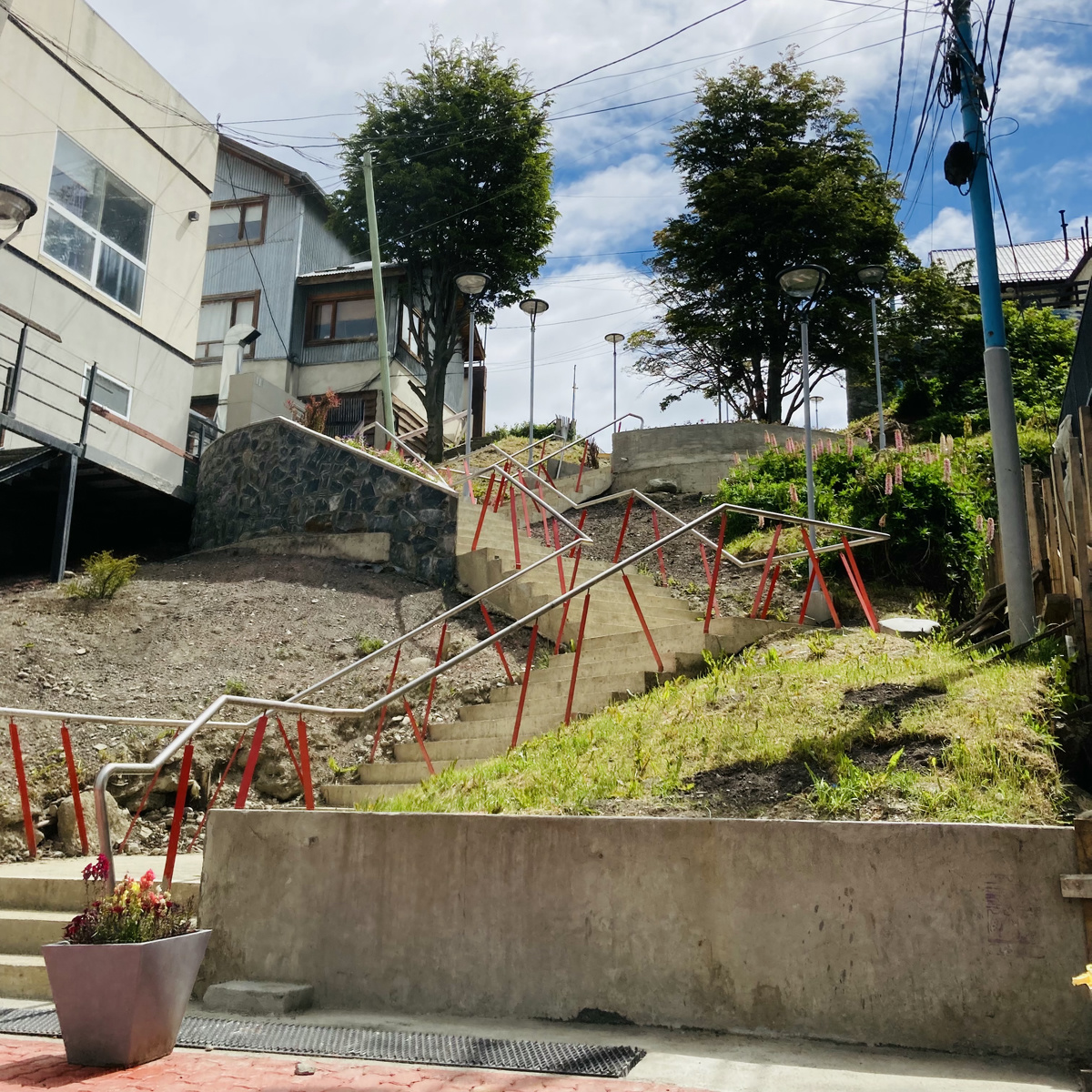 A funky red trim staircase on a hill. The sky above is blue, and generic buildings surround the hill.