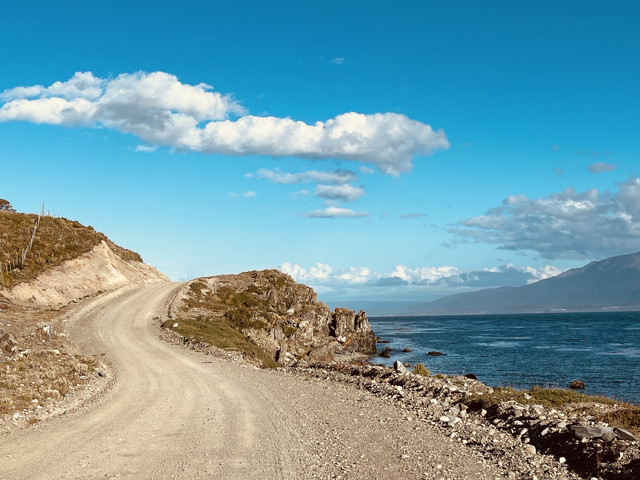 A beautiful winding gravel road next to shining blue water.