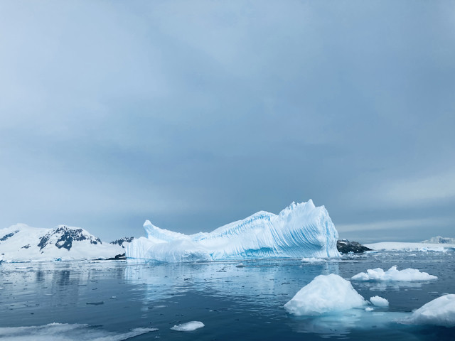 A striking blue glacier floats in Antarctic waters. The glacier has a series of ridges cut into it.